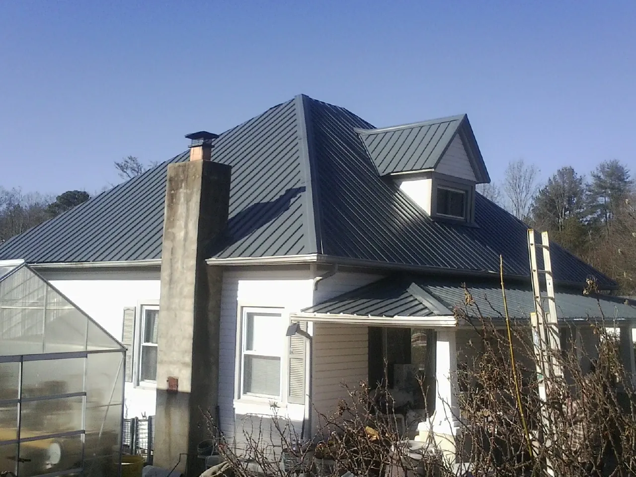Dark blue standing seam metal roof on a white farmhouse with dormer — Slate & Tile Roof Repair by Roofing Brothers in Dalton