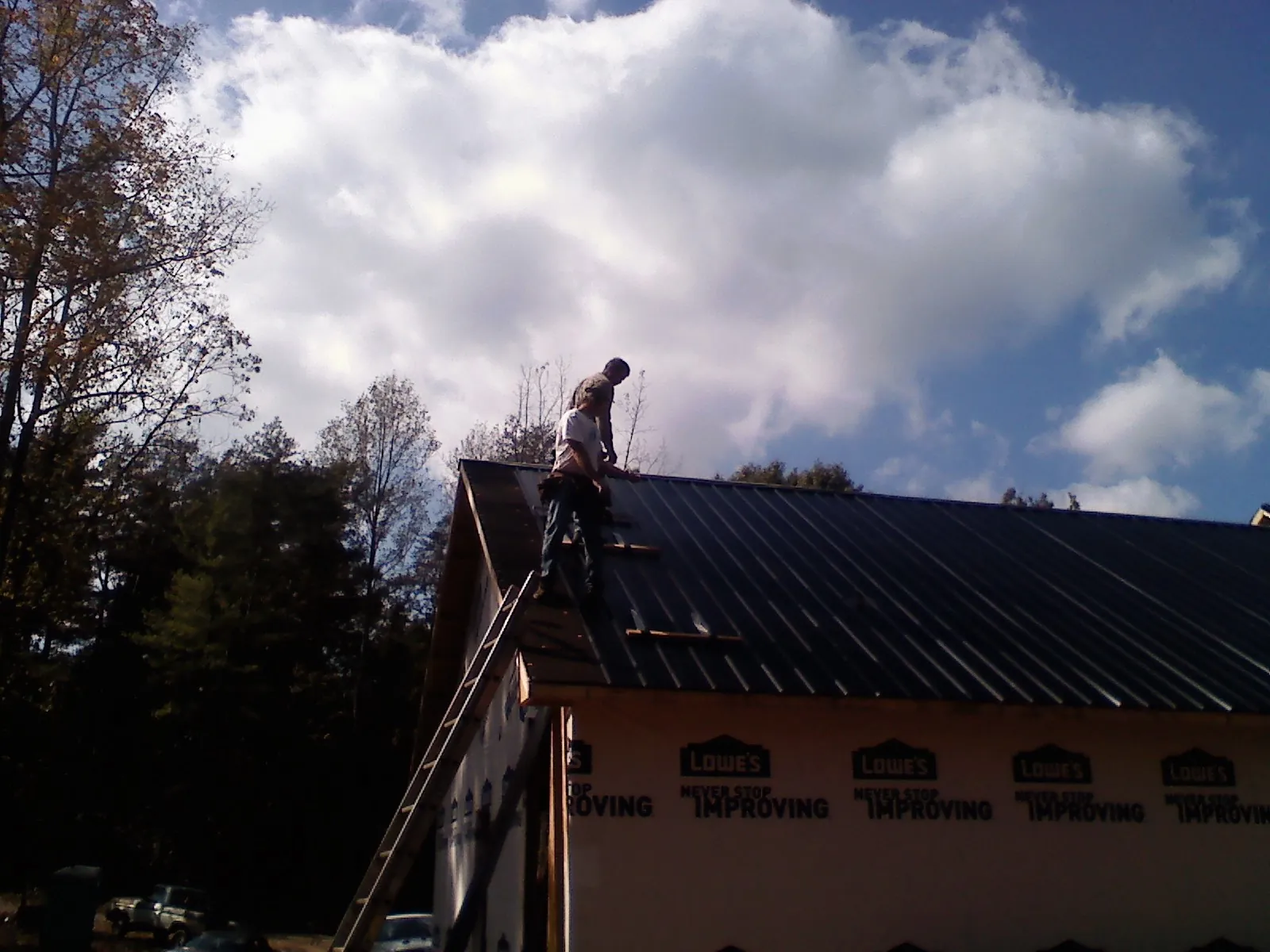 Roofer fastening dark metal panels high against a cloudy sky, from a Roof Inspection job in Dalton